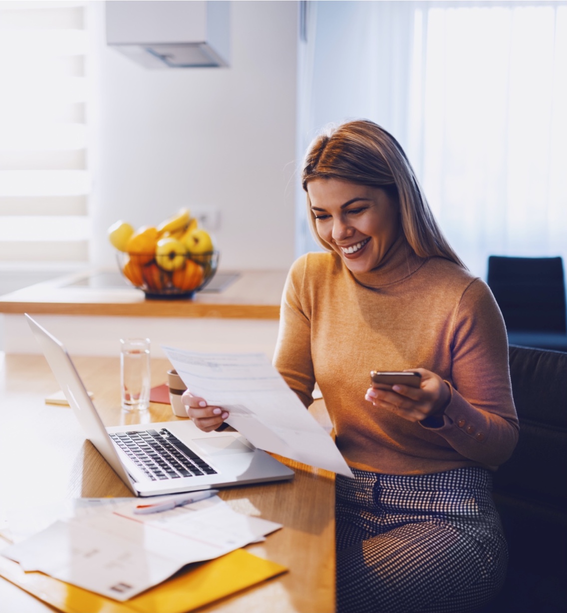 woman reading papers over laptop happily