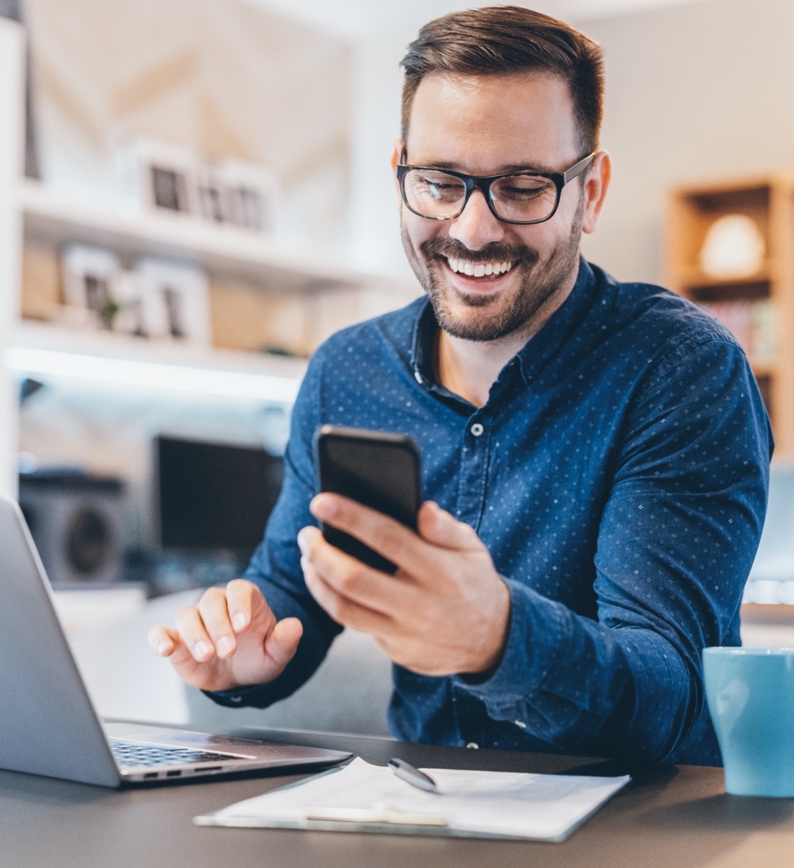 man checks phone while working on laptop