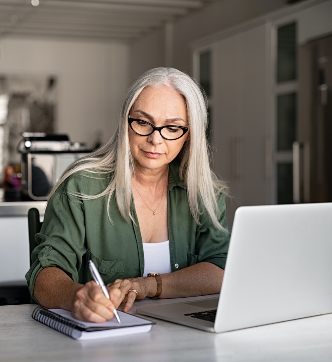 a woman writes while working on laptop