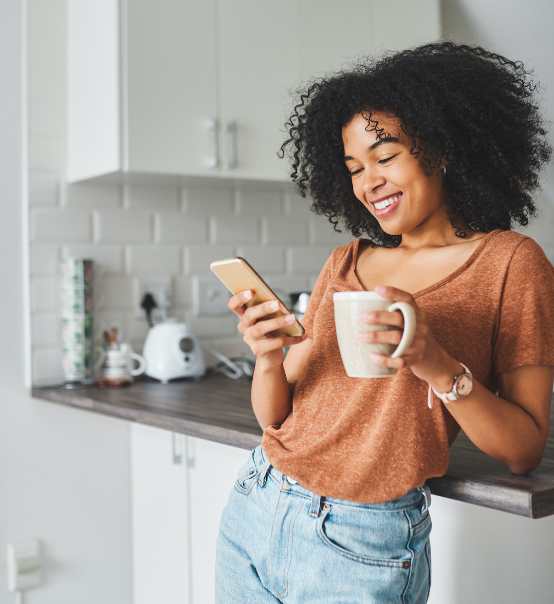 Shot of a young woman using a smartphone and having coffee in the kitchen at home